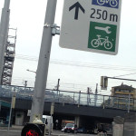 Schild am Fahrradampelmast mit Piktogrammen Radgarage und Radservice, Entfernungsangabe und Richtungspfeil